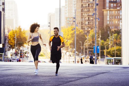 happy man and sports woman running in the city street with buildings in the background. urban sports workout in couple and healthy lifestyle concept