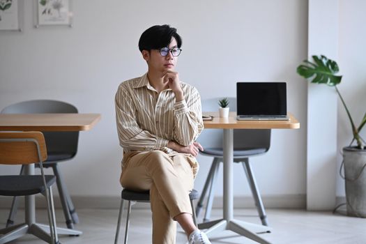 Thoughtful businessman sitting in comfortable workplace and looking out of window.