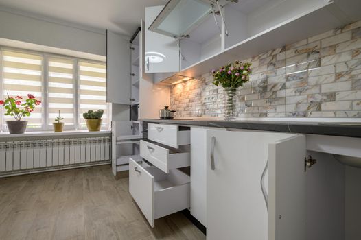 Interior renovation showcase of well designed modern trendy white kitchen, cabinet doors open, drawers retracted