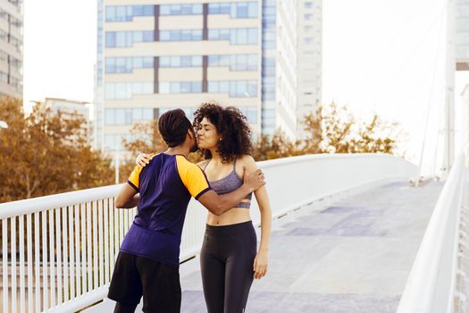 athletic latin woman and sporty black man greeting each other before running together in a city bridge with buildings in the background. urban sports workout in couple and healthy lifestyle concept
