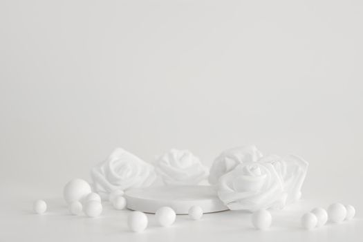 White marble podium on the white background with pearls and flowers. Podium for product, cosmetic presentation. Creative mock up. Pedestal or platform for beauty products