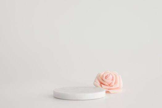 White marble podium on the white background with pink flowers. Podium for product, cosmetic presentation. Creative mock up. Pedestal or platform for beauty products
