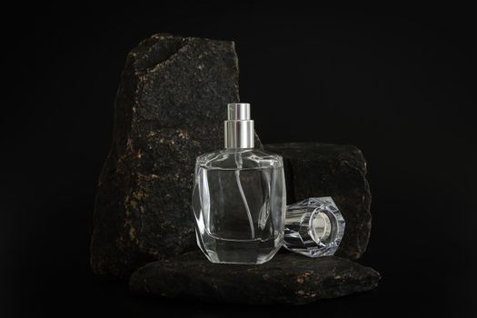 Unbranded perfume bottle standing on stone podium. Perfume presentation on the black background. Mockup. Trending concept in natural materials. Women's and men's essence. Natural cosmetic
