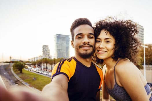 selfie of latin woman and sports man during a rest in the workout through the city at dusk, mobile phone view, technology in sport and healthy lifestyle concept