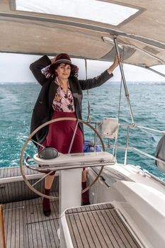 Attractive middle-aged woman at the helm of a yacht on a summer day. Luxury summer adventure, outdoor activities