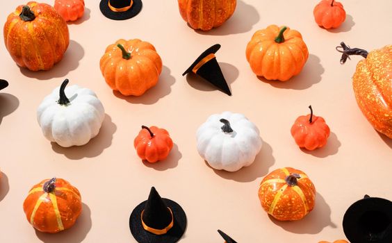 Pumpkin pattern, decorative pumpkins and halloween hats on orange high angle view. Autumn, fall, halloween concept. Trend shadow.