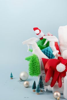 Christmas cleaning. Cleaning tools and Christmas decorations in white laundry basket on blue background with copy space