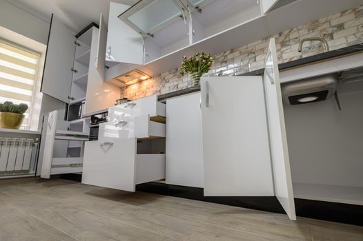 Interior renovation showcase of well designed modern trendy white kitchen, cabinet doors open, drawers retracted, low angle view