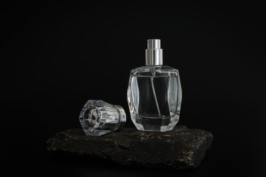 Unbranded perfume bottle standing on stone podium. Perfume presentation on the black background. Mockup. Trending concept in natural materials. Women's and men's essence. Natural cosmetic