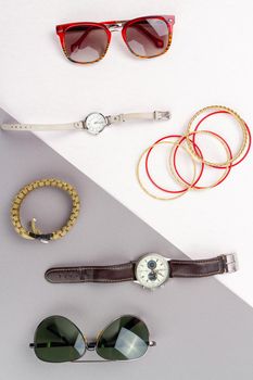 Flat lay contrast of mens and womens accessories. Top view glasses with watch and bracelets.