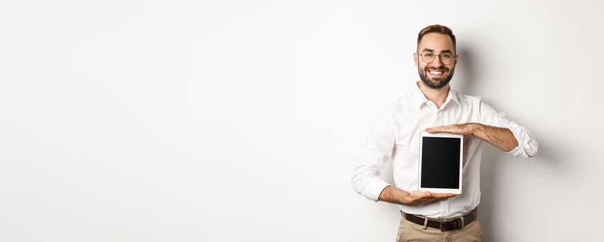 Smiling manager showing something on digital tablet screen, demonstrating website, standing over white background.