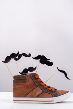 Vertical shot of brown sneaker with cartoon moustaches. Mens shoe with copy space on white.
