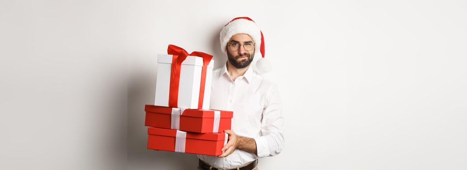 Merry christmas, holidays concept. Thoughtful man holding xmas gifts and looking suspicious at camera, celebrating New Year, white background.