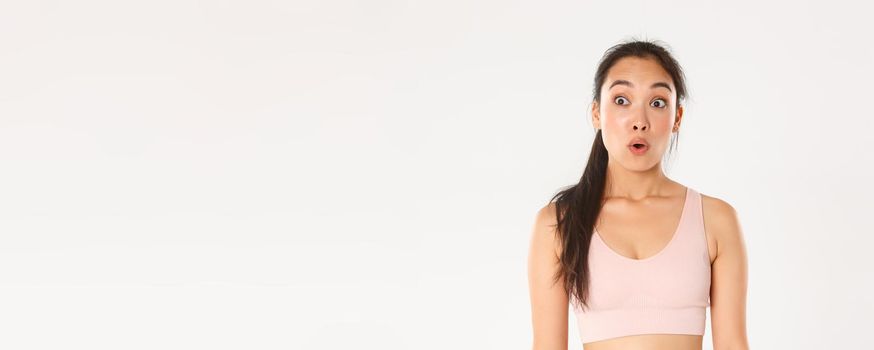 Sport, wellbeing and active lifestyle concept. Close-up of excited and amazed asian fitness girl, cute brunette in sportsbra say wow, gasping and looking left at your logo or promo banner.