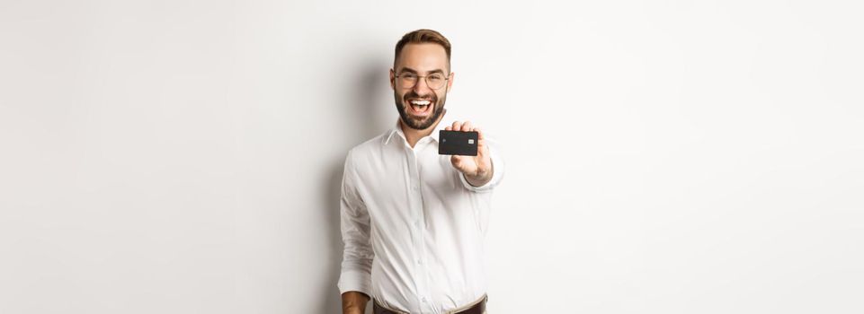 Excited caucasian man in glasses showing credit card, concept of shopping.