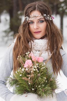 Beautiful bride in a white dress with a bouquet in a snow-covered winter forest. Portrait of the bride in nature.