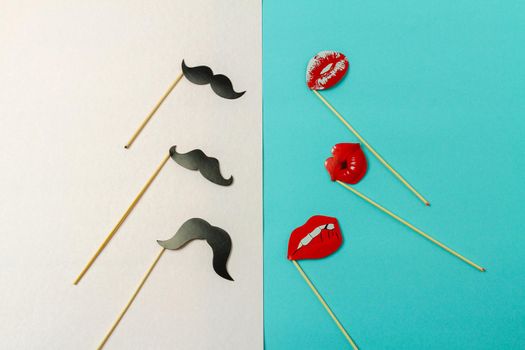 Paper moustaches and lips on wooden sticks. White and turquoise background.