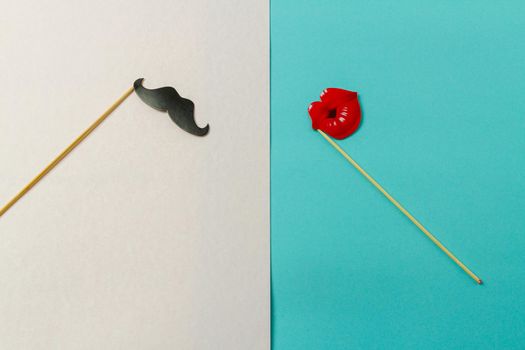 Paper moustache and lips on wooden sticks. Concept of couple or contrast. White and turquoise background.