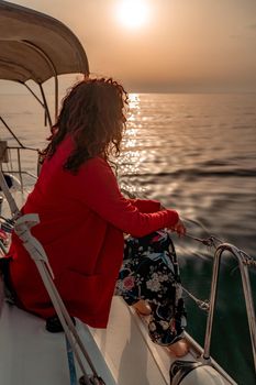 A woman sits on the bow of a yacht on a sunny summer day, the breeze develops her hair, a beautiful sea is in the background.