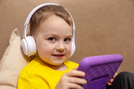 Happy little boy with yellow shirt playing game on digital tablet at home. Portrait of a child at home watching cartoon on violet tablet. Modern kid and education technology