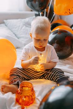 Children's Halloween - a boy in a carnival costume with orange and black balloons at home. Ready to celebrate Halloween.