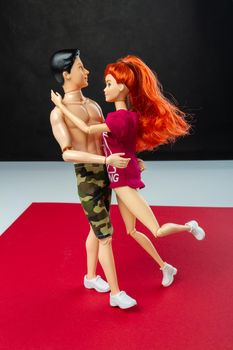 Hugging couple dolls on red surface. Ginger Barbie and Ken.