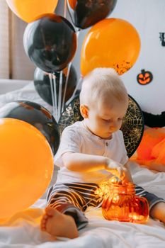 Children's Halloween - a boy in a carnival costume with orange and black balloons at home. Ready to celebrate Halloween