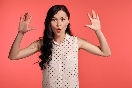 Studio shot of a good-looking teeny girl, wearing casual white polka dot blouse. Little brunette female gesticulating posing over a pink background. People and sincere emotions.