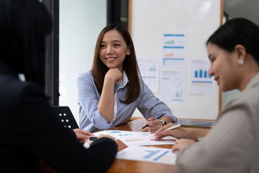 A young asian woman is having a business meeting with her team colleagues in a conference room