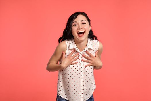 Studio shot of an adorable teeny girl, wearing casual white polka dot blouse. Little brunette female smiling and looking at the camera posing over a pink background. People and sincere emotions.