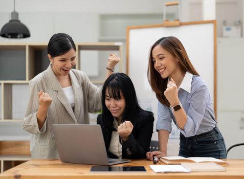 Happy business asian people are keeping arms raised hi five and expressing joyful while standing. achieving goals