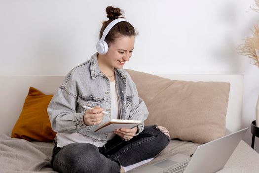 Young beautiful woman with casual clothes sitting on the bed at home with laptop computer and studying. Girl using e-learning platform to make a video call with her teacher. Distance education