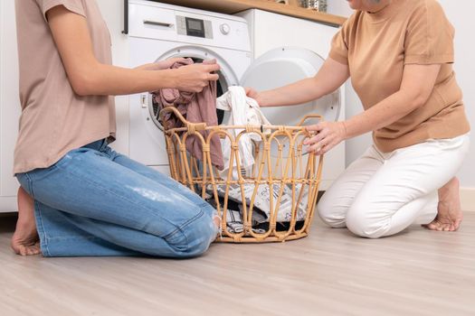 Daughter and mother working together to complete their household chores near the washing machine in a happy and contented manner. Mother and daughter doing the usual tasks in the house.