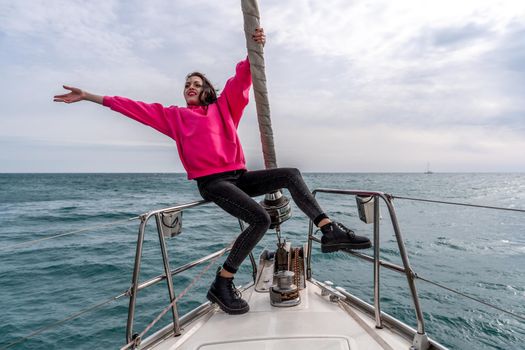 Woman standing on the nose of the yacht at a sunny summer day, breeze developing hair, beautiful sea on background.