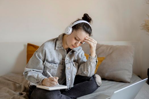 Young beautiful woman with casual clothes sitting on the bed at home with laptop computer and studying. Girl using e-learning platform to make a video call with her teacher. Distance education