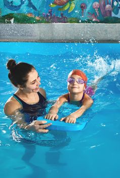 Little girl learning to swim in indoor pool with pool board. Swimming lesson. Active child swims in water