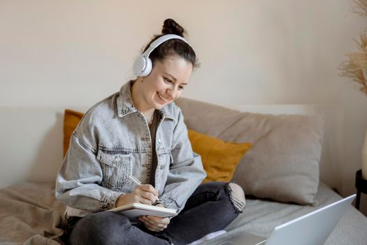 Young beautiful woman with casual clothes sitting on the bed at home with laptop computer and studying. Girl using e-learning platform to make a video call with her teacher. Distance education