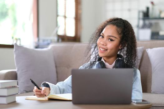 Portrait of happy female student with dark skin smiling at camera. cheerful African American hipster girl enjoying e learning and preparation to course work.