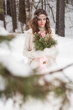 Beautiful bride in a white dress with a bouquet in a snow-covered winter forest. Portrait of the bride in nature.