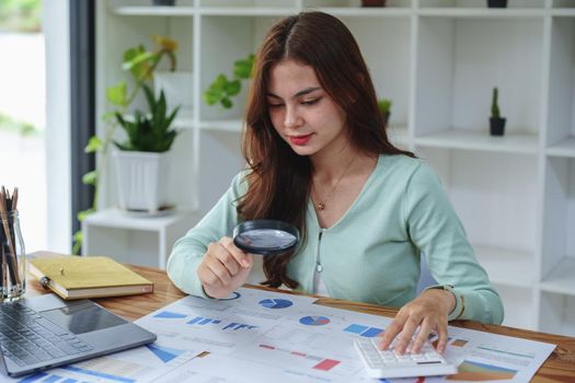 A half-bred girl, an audit employee, an accountant holding a magnifying glass and using a calculator to check the financial statement documents to calculate the annual tax payment to the IRS.