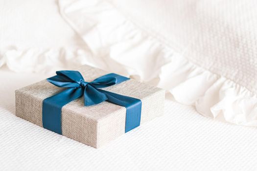 Holiday present and luxury online shopping delivery, wrapped linen gift box with blue ribbon on bed in bedroom, chic countryside style, close-up