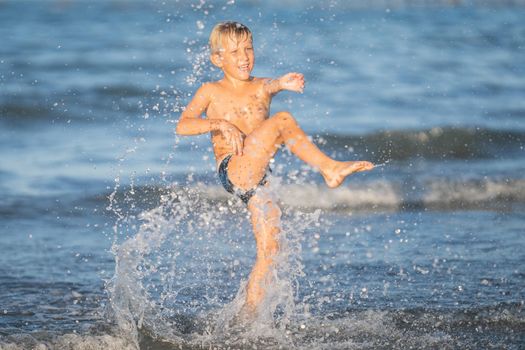 Blond little child in the water making splashes,happy kid enjoying on the beach resort, summer concept holiday, Emilia Romagna, Italy.