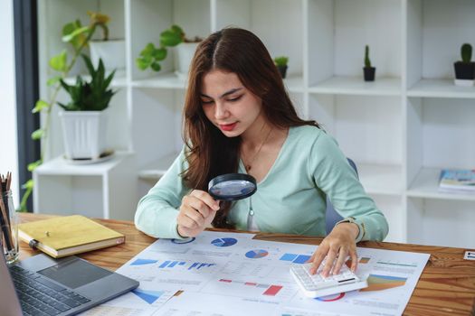 A half-bred girl, an audit employee, an accountant holding a magnifying glass and using a calculator to check the financial statement documents to calculate the annual tax payment to the IRS.