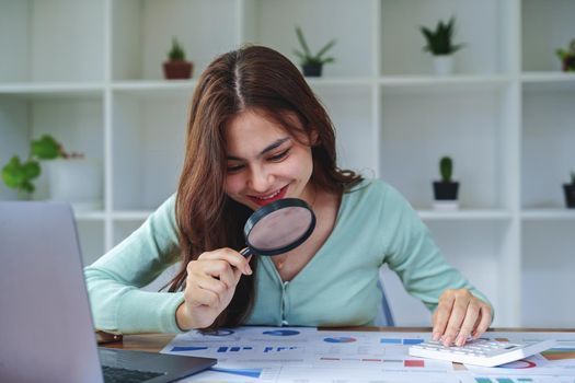 A half-bred girl, an audit employee, an accountant holding a magnifying glass and using a calculator to check the financial statement documents to calculate the annual tax payment to the IRS.