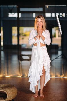 Portrait of a smiling girl in a white dress with her palms clasped in front of her.