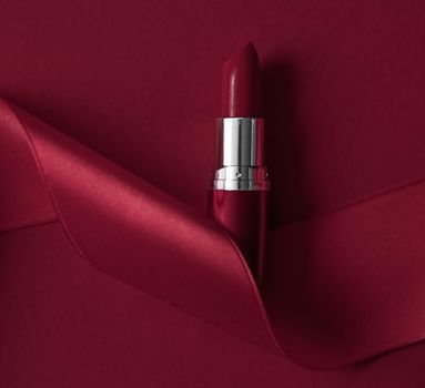 Cosmetic branding, glamour lip gloss and shopping sale concept - Luxury lipstick and silk ribbon on maroon holiday background, make-up and cosmetics flatlay for beauty brand product design