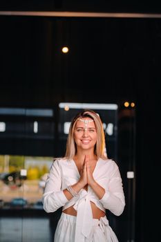 Portrait of a smiling girl in a white dress with her palms clasped in front of her.