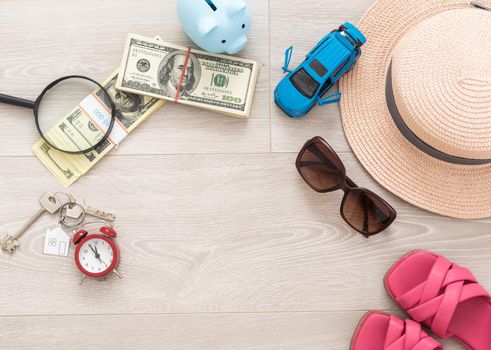 A piggy bank with dollar bills in a travel setting. In the composition of the image: Sun Hat, Alarm Clock. Concept of saving money for traveling on vacation