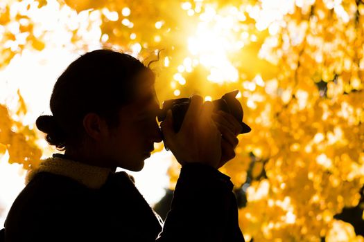 Silhouette of a male photographer under a fall tree with bright yellow leaves