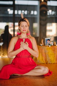 Meditation and concentration. a woman in a red dress, sitting on the floor with her eyes closed, is practicing medicine indoors. Peace and relaxation.